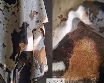 May include: Cowhide textile with a natural pattern of brown, black, and white spots. The material is draped, showcasing its texture and color variations. The image includes a close-up view of the hide's surface and a designer's logo.