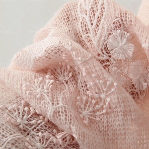 Puede incluir: Primer plano de una delicada tela de encaje rosa pálido. La tela presenta intrincados bordados florales y un tejido transparente y abierto. La textura suave y el color sutil sugieren una estética romántica o vintage, adecuada para prendas de vestir o proyectos de artesanía.