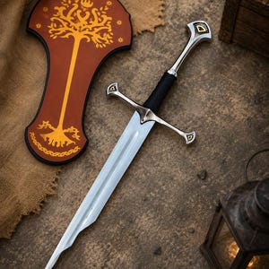 Op de afbeelding: Een zilverkleurig metalen zwaard met een zwart handvat en een pareerstang met kleine rode accenten. Naast het zwaard ligt een bruine, schildvormige plaat versierd met een goudkleurig boomontwerp, een kroon en stermotieven.