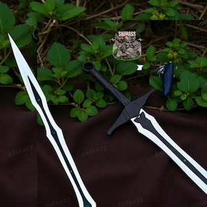 May include: Two swords with white blades and black accents are displayed against a backdrop of green foliage and a brown surface. The swords have black handles and crossguards. The blades have a central black stripe.