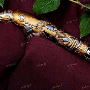 May include: A gold and silver decorative sword handle with intricate carvings. The handle is shaped like a bird's head with a beak.