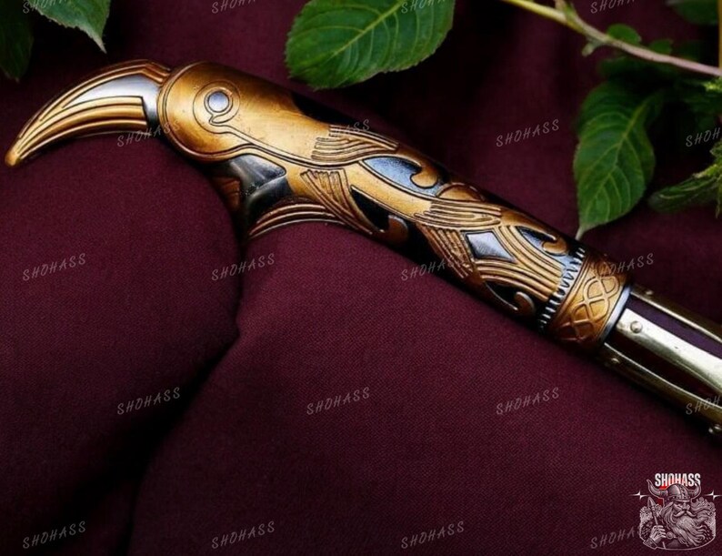 May include: A gold and silver decorative sword handle with intricate carvings. The handle is shaped like a bird's head with a beak.