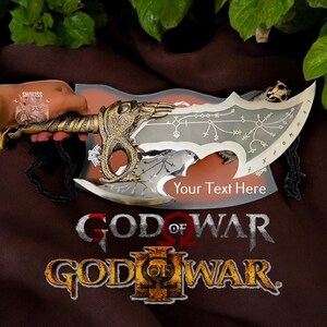 May include: A silver and gold replica of the Blades of Chaos from the God of War video game series. The blades are held by a hand and feature intricate details and the text "Your Text Here".