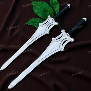 May include: Two silver swords with black handles are displayed on a brown cloth, with green leaves. The swords have a distinctive design on the hilt and a sharp blade. The brand name "SHOHASS" is visible.