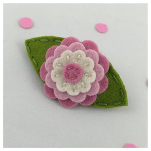 May include: A felt flower brooch with a pink and white flower with a green leaf.