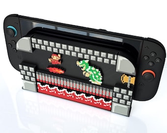 May include: Black gaming console with a pixelated Super Mario Bros. design. The design features Mario, a Koopa Troopa, and other elements from the classic video game. The console has black controllers with blue and orange accents.