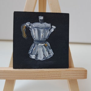 May include: A white and blue painted metal coffee pot with a gold handle on a black background.