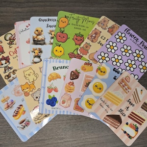 May include: A selection of sticker sheets with diverse designs. The stickers showcase charming illustrations of animals, food, and flowers. Some sheets include text such as "Cut," "Brunch," and "Flower Power." The stickers are displayed on a wooden surface.