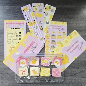 May include: A collection of lemon-themed stationery items including a clear glittery zipper pouch with square stickers, two vertical bookmarks with holographic circles, and three rectangular cards featuring lemonade menu text and savings trackers.