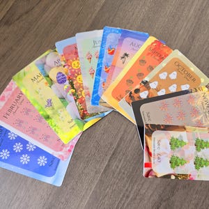 May include: Twelve colourful cards with a different month of the year on each card. Each card has a different design and a price tag. The cards are arranged in a semi-circle.