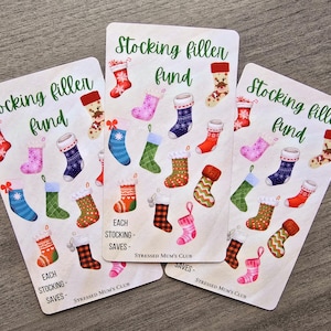 May include: Three printable cards with a Christmas stocking theme. Each card has the text "Stocking filler fund" and features illustrations of colourful stockings with different patterns. The text "Each stocking saves" is also included on each card.