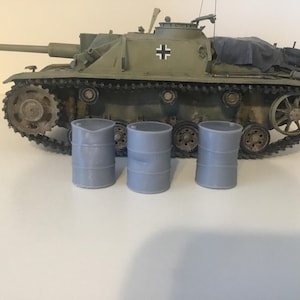 May include: A model of a military tank in olive green with black tracks and a long gun barrel. Three small, gray barrels are in front of the tank. The tank has a black and white cross symbol.