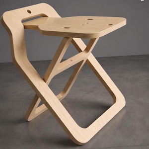 May include: A light-colored wooden folding stool with a unique design. The stool features a square seat with rounded corners and a curved backrest. The legs form an X-shape when folded. The stool is made of light-colored wood.