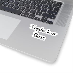 May include: A white sticker with the text "Topdeck or Bust" in a black, elegant font. The sticker is placed on a silver laptop, with the keyboard visible in the background.