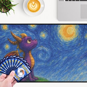 May include: A large rectangular mousepad featuring a purple dragon with yellow horns and wings, set against a starry night sky in the style of Van Gogh. A hand holds a fan of Pokemon trading cards. The mousepad is on a white surface.