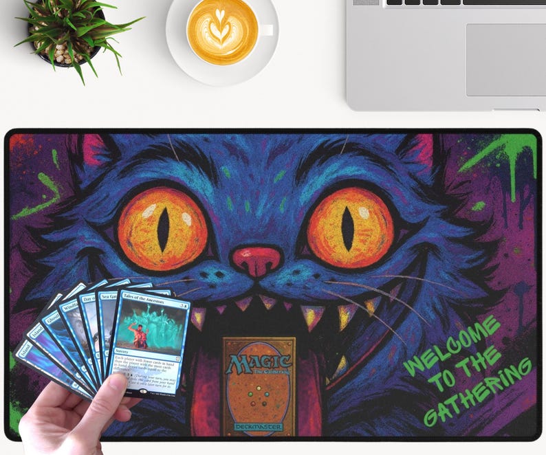 K&ouml;nnte beinhalten: Rechteckige Magic: The Gathering Spielmatte mit einem blauen Katzendesign, orangefarbenen Augen und scharfen Z&auml;hnen. Auf der Matte steht der Text "WELCOME TO THE GATHERING". Eine Hand h&auml;lt Magic-Karten.