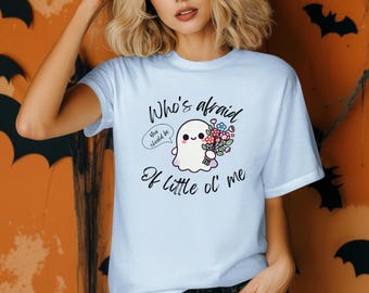 以下が含まれることがあります： 「Who's afraid of little ol' me」の文字と、花束を持った漫画のゴーストが描かれた水色のTシャツ。ゴーストは「You should be」という吹き出しを持っています。