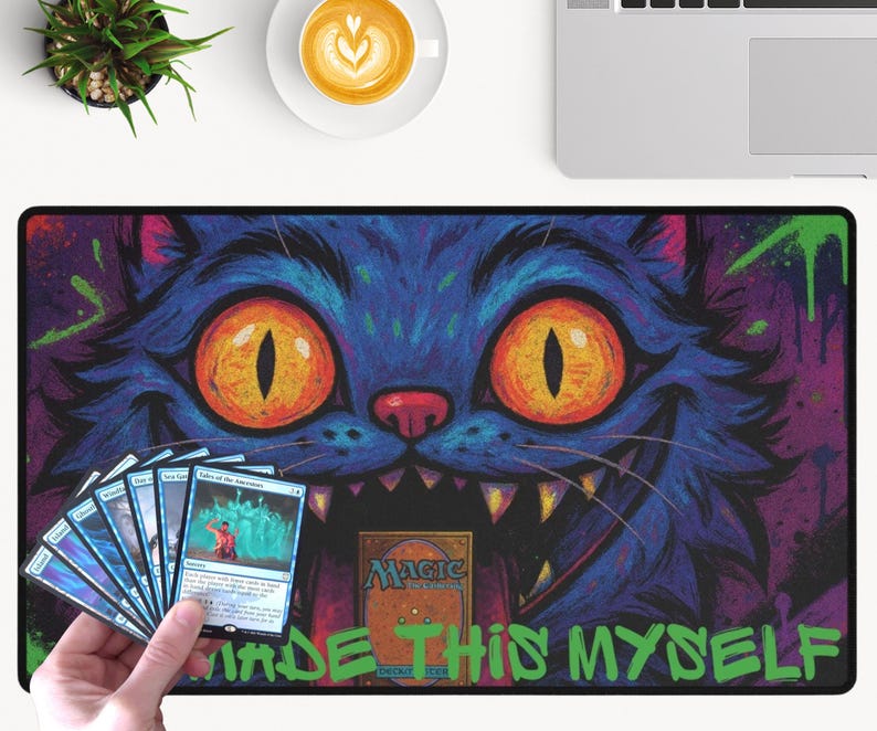 May include: A Magic the Gathering playmat with a blue cat design, orange eyes, and sharp teeth. The mat has the text "MADE THIS MYSELF" in green. A hand holds a stack of Magic the Gathering cards. The background is purple.