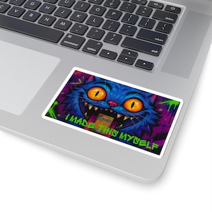 Peut inclure: Un autocollant avec un chat de dessin animé souriant, aux yeux orange et à la fourrure bleue, sur un fond violet et vert. Le texte "I MADE THIS MYSELF" est en vert.