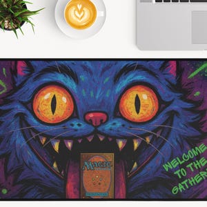 K&ouml;nnte beinhalten: Rechteckige Schreibtischunterlage mit einem Cartoon-Katzen-Design. Die Katze ist &uuml;berwiegend blau mit orangefarbenen Augen und einem breiten Grinsen. Der Text "WELCOME TO THE GATHERING" ist sichtbar, mit einer Magic-Karte in der Mitte. Das Design hat rosa und lila Akzente.