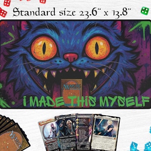 May include: A rectangular playmat with a grinning blue cat face design, measuring 60cm x 35cm. The mat features the text "I MADE THIS MYSELF" and a Magic: The Gathering card. Several Magic cards and dice are visible.