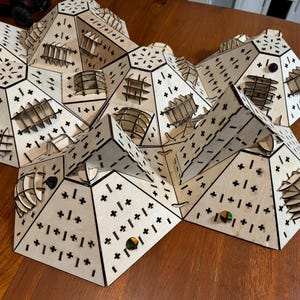 May include: A wooden game board with a geometric design. The board is made up of multiple triangular pieces that fit together to create a larger shape. The board is decorated with black lines and plus signs. There are small, colorful game pieces on the board.