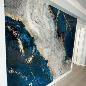 Könnte beinhalten: Große Wandkunst mit einem abstrakten Design in Blau-, Grau- und Goldtönen. Das Kunstwerk hat eine glänzende Oberfläche und ist an einer weiß gerahmten Wand angebracht. Das Design ähnelt Marmor oder Achat.