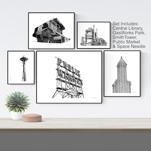May include: A set of five black and white illustrations of iconic Seattle landmarks, including the Central Library, Gas Works Park, Smith Tower, Public Market, and the Space Needle. The illustrations are framed and displayed on a white wall.