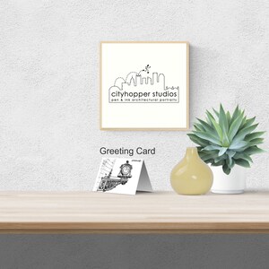 Puede incluir: Una impresión enmarcada con una ilustración de horizonte en blanco y negro y el texto "cityhopper studios pen & ink architectural portraits". Una tarjeta de felicitación con un dibujo arquitectónico en blanco y negro se muestra sobre una superficie de madera, con un jarrón amarillo y una planta suculenta en maceta.