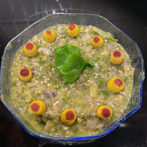 May include: A bowl of green salsa with yellow and red flower buds on top.
