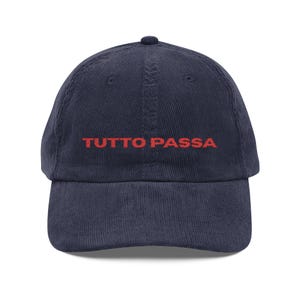 Peut inclure: Casquette de baseball en velours côtelé bleu marine avec le texte rouge "TUTTO PASSA" brodé sur le devant. La casquette a une visière incurvée et une sangle réglable à l'arrière.