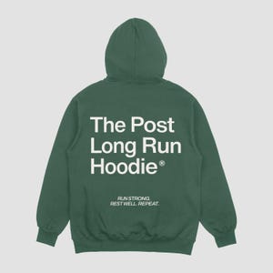 Può includere: Una felpa con cappuccio verde scuro con maniche lunghe. La parte posteriore mostra il testo bianco "The Post Long Run Hoodie" e lo slogan "Run Strong. Rest Well. Repeat."