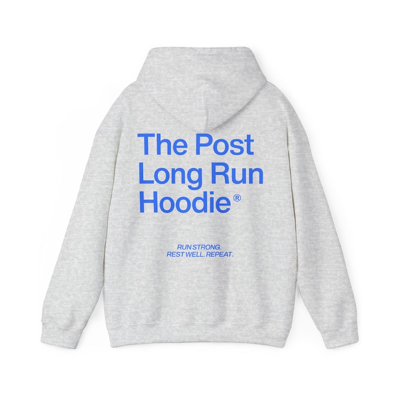 May include: A light gray hoodie with a hood and long sleeves. The back of the hoodie features the text "The Post Long Run Hoodie" in blue, with the words "Run Strong. Rest Well. Repeat." printed below.