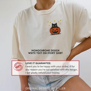 Może przedstawiać: Kremowa koszulka z czarnym kotem siedzącym na pomarańczowej dyni i ż&oacute;łtymi gwiazdami. Koszulka ma napis "MONOCHROME DESIGN WHITE TEXT ON IVORY SHIRT". Pokazana jest r&oacute;wnież gwarancja.
