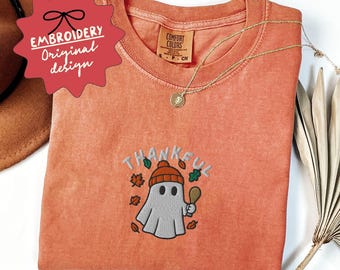 May include: Orange Comfort Colors t-shirt with an embroidered design featuring a ghost wearing a beanie and holding a spoon, with the word "THANKFUL". A gold necklace is draped across the shirt. The shirt has a vintage look.