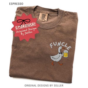 May include: Espresso-colored t-shirt with an embroidered design of a goose holding a beer mug, with the word "FUNCLE" above it. The shirt has a Comfort Colors tag and a red "EMBROIDERY" sticker. The text "Original Design by Seller" is also visible.