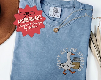 May include: A blue Comfort Colors t-shirt featuring an embroidered goose carrying a jar, with the text "DON'T GET ME STARTED". A gold necklace and a red "EMBROIDERY" tag are also visible.