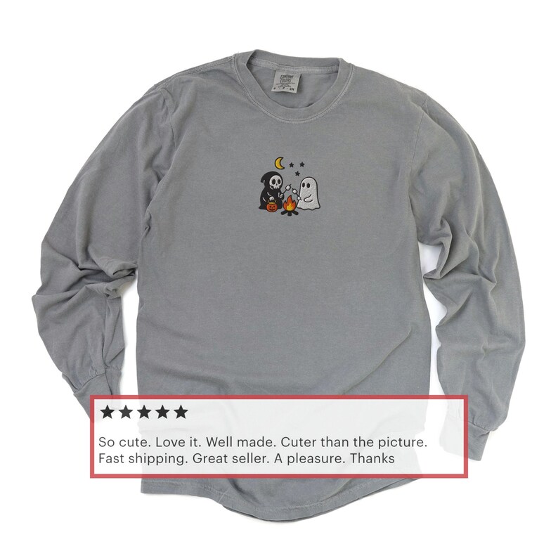 May include: Gray long-sleeve shirt with a small embroidered Halloween design featuring a ghost, a grim reaper, and a campfire. The shirt has a crew neck and a relaxed fit. The shirt is made of a soft, comfortable material.