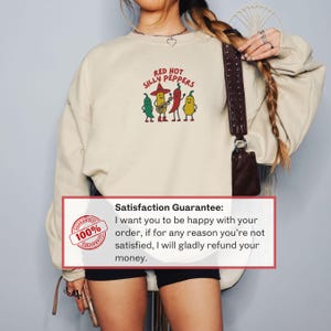 K&ouml;nnte beinhalten: Beige Sweatshirt mit dem Text "RED HOT SILLY PEPPERS" und einer Cartoon-Grafik von vier anthropomorphen Paprika. Das Sweatshirt hat einen Rundhalsausschnitt und lange &Auml;rmel.