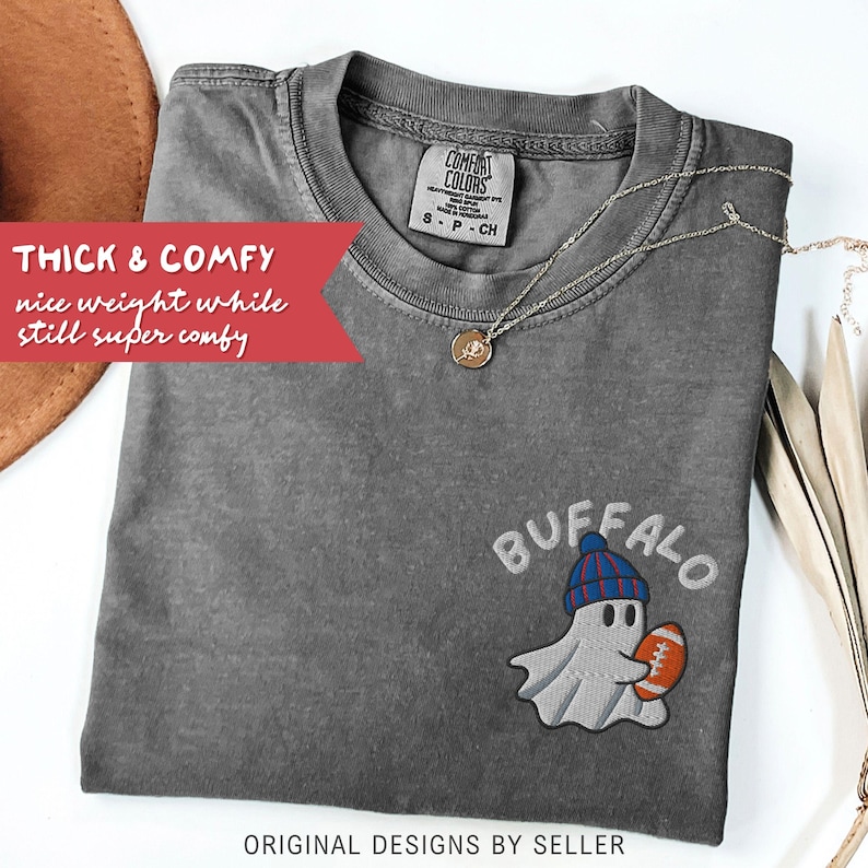 May include: A gray Comfort Colors t-shirt with an embroidered ghost wearing a blue and red hat and holding a football. The word "BUFFALO" is embroidered above the ghost. The text "THICK & COMFY" is on a red banner.