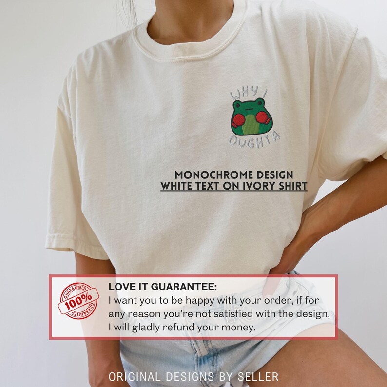 May include: Ivory-colored t-shirt featuring a green frog wearing red boxing gloves, with the text "WHY I OUGHTA." Below the graphic, the shirt reads "MONOCHROME DESIGN WHITE TEXT ON IVORY SHIRT." The shirt has a crew neck and short sleeves.