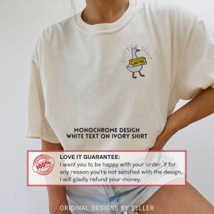 以下が含まれることがあります： バターを持ったガチョウの漫画が描かれたアイボリー色のTシャツ。テキストは「BUTTER SLUT」と書かれています。シャツには「MONOCHROME DESIGN WHITE TEXT ON IVORY SHIRT」という文字も書かれています。