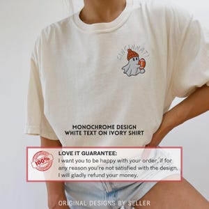 May include: Cream-coloured t-shirt featuring a small graphic of a ghost wearing a beanie and holding a football, with the word "Cincinnati" above. The text "MONOCHROME DESIGN WHITE TEXT ON IVORY SHIRT" is also visible.