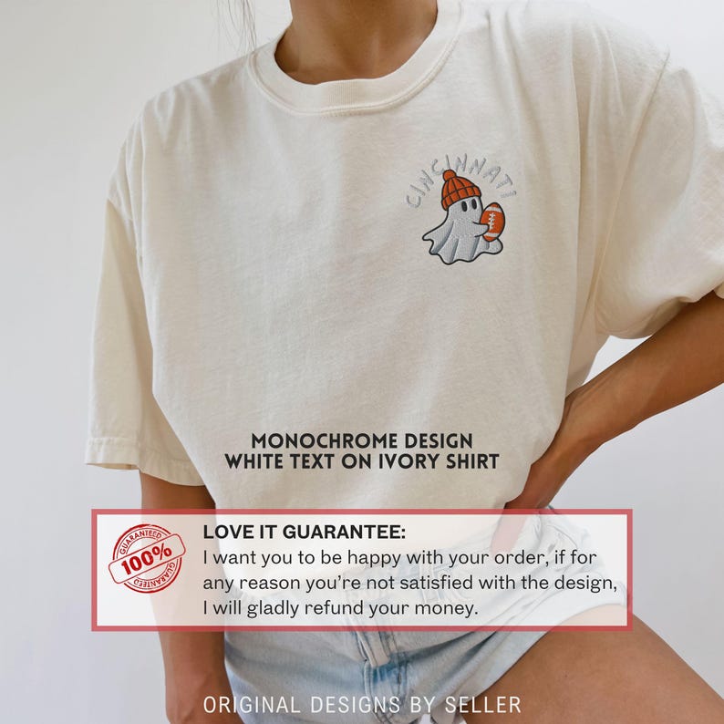 May include: Cream-coloured t-shirt featuring a small graphic of a ghost wearing a beanie and holding a football, with the word "Cincinnati" above. The text "MONOCHROME DESIGN WHITE TEXT ON IVORY SHIRT" is also visible.