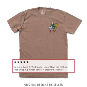 May include: A brown t-shirt with a cartoon goose wearing a "57" jersey. The goose is white with a green "5" and a yellow "7". The text "ORIGINAL DESIGNS BY SELLER" is at the bottom.