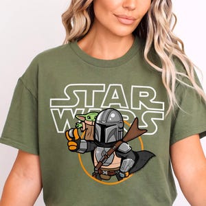 May include: A green t-shirt with a white "Star Wars" graphic featuring a cartoon Mandalorian and Grogu.