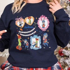 May include: Navy blue sweatshirt featuring Zootopia characters in framed designs. The design includes Judy Hopps and Nick Wilde, with the word "Zootopia" and the word "Welcome" in a circular pattern. The word "NAVY" is printed on the bottom left.