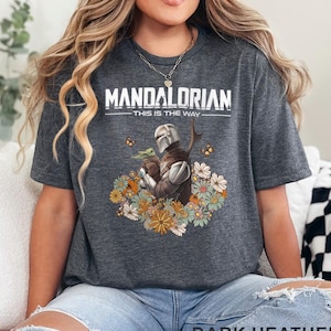 May include: Dark heather grey t-shirt featuring a floral design with The Mandalorian and Grogu. The text "Mandalorian - This is the Way" is printed on the shirt.