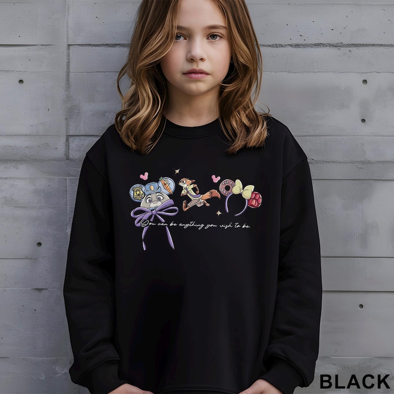 Puede incluir: Sudadera negra con dise&ntilde;os de personajes de dibujos animados coloridos y el texto "You can be anything you wish to be". El dise&ntilde;o incluye un rat&oacute;n con un lazo, un zorro y unas orejas con una rosquilla y frambuesas.
