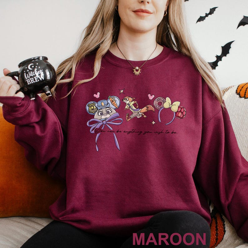 Puede incluir: Sudadera granate con un dise&ntilde;o de dibujos animados con un conejo, un zorro y una diadema. El texto "You can be anything you wish to be" est&aacute; impreso debajo del dise&ntilde;o. La palabra "MAROON" est&aacute; impresa en la parte inferior.